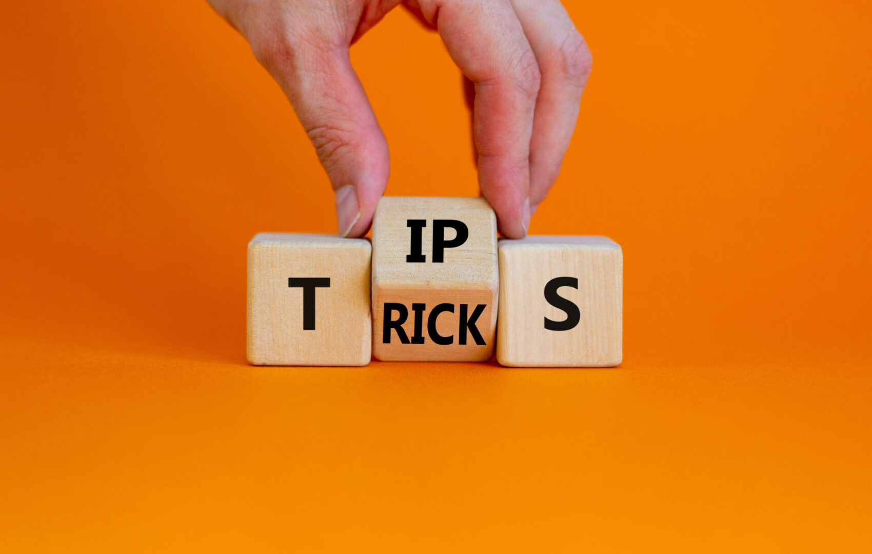 Tips and tricks symbol. Businessman turn the wooden cube and changes the word 'tips' on 'tricks'. Beautiful orange background. Business and tips and tricks concept, copy space. Tips and tricks symbol. Businessman turn the wooden cube and changes the word 'tips' on 'tricks'. Beautiful orange background. Business and tips and tricks concept, copy space.