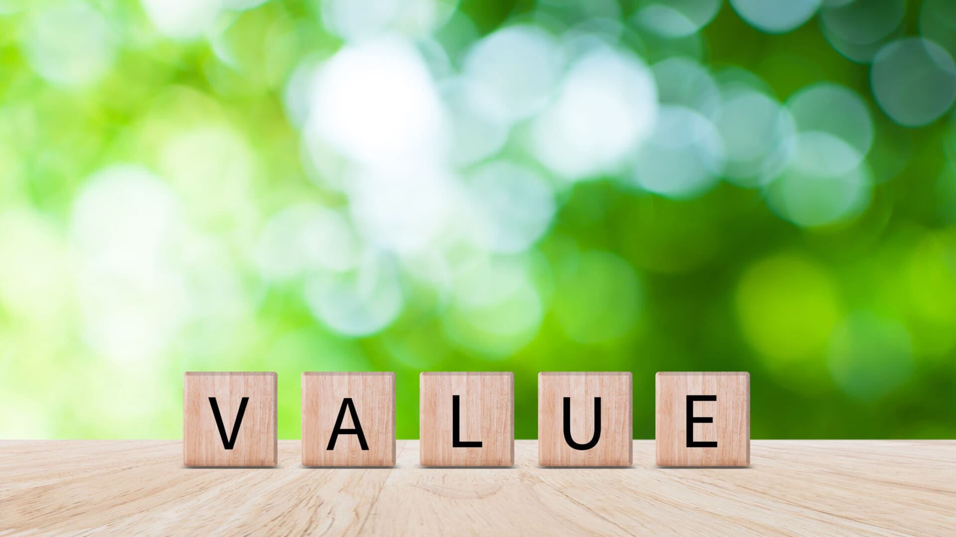 Wooden blocks spelling the word 'VALUE' on a table with a blurred green background.