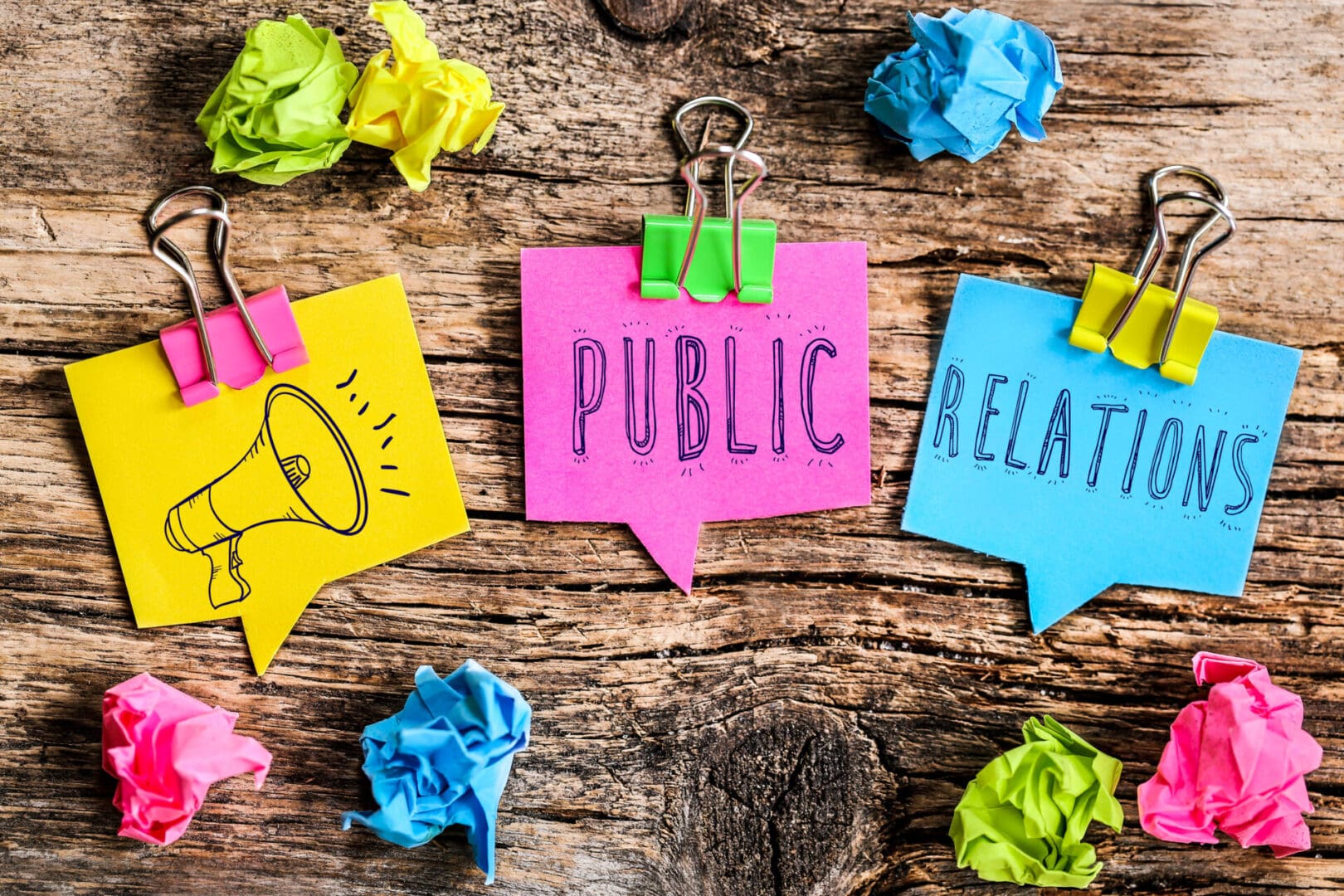 Colorful sticky notes with the words Public, Relations, and a megaphone icon on a wooden surface.