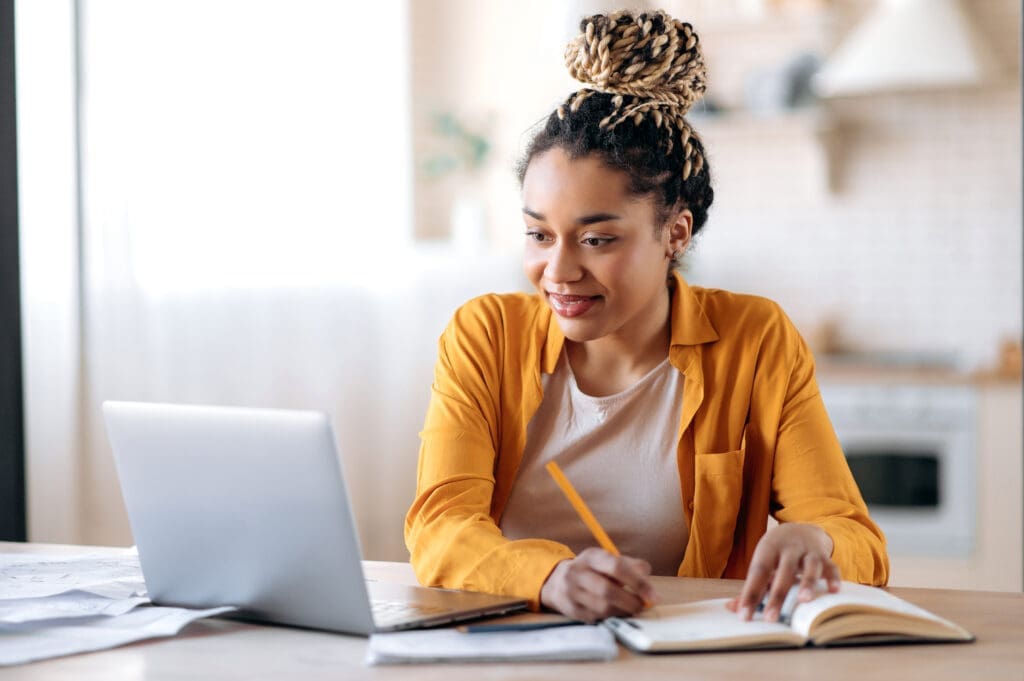 Young woman studying with a laptop and notebook at home.