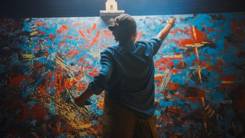 Person painting an abstract, colorful mural with expressive brushstrokes.